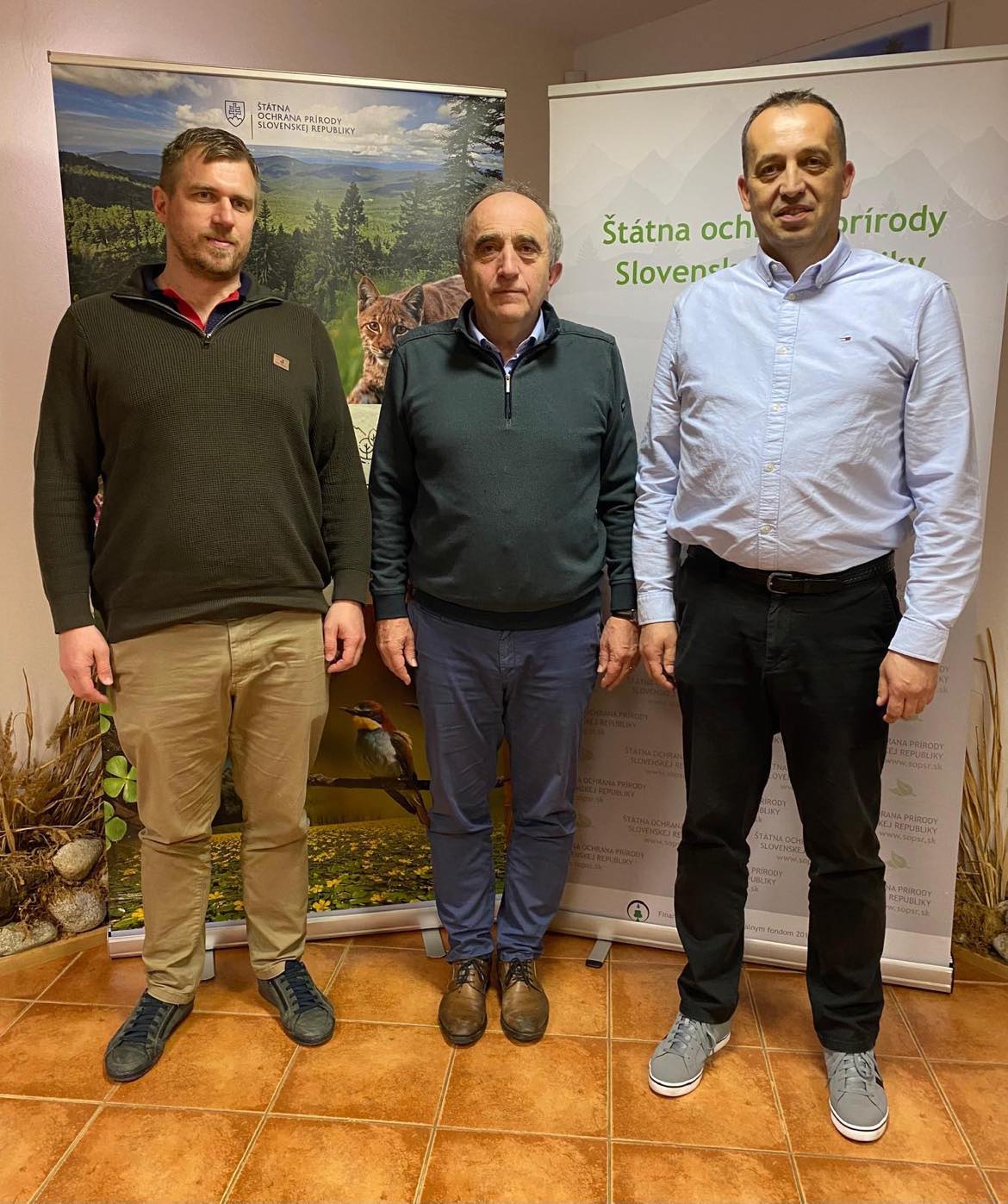 Traja muži stoja vedľa seba pred informačnými panelmi Štátnej ochrany prírody Slovenskej republiky. Za nimi sú bannery s prírodnými motívmi – rysom a vtákom v mokradi.