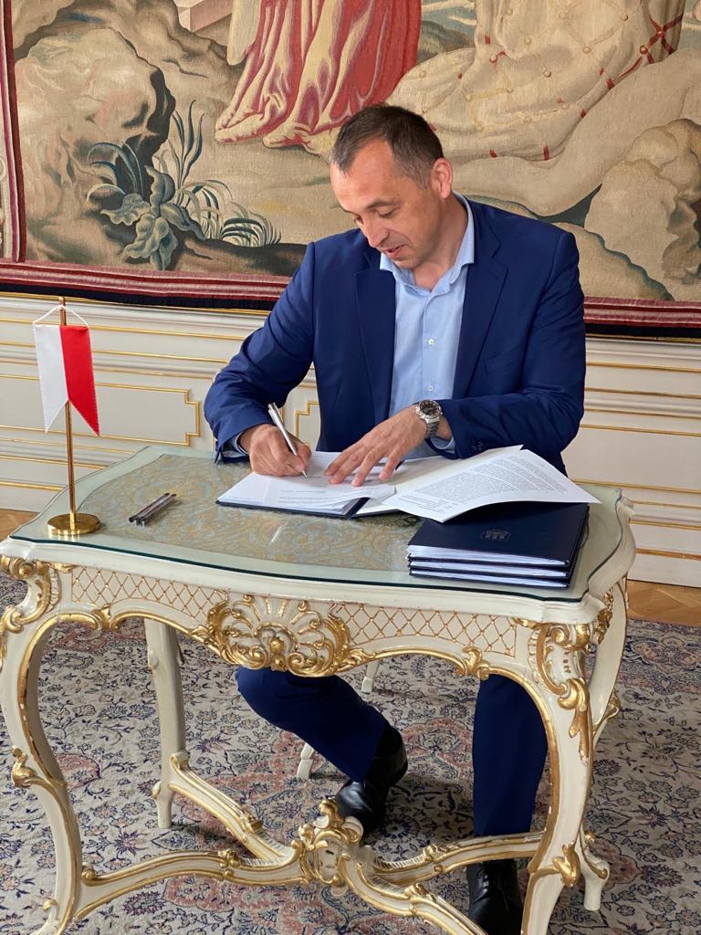 Generálny riaditeľ ŠOP SR v modrom obleku podpisuje dokumenty pri ozdobnom stole s malou vlajočkou.