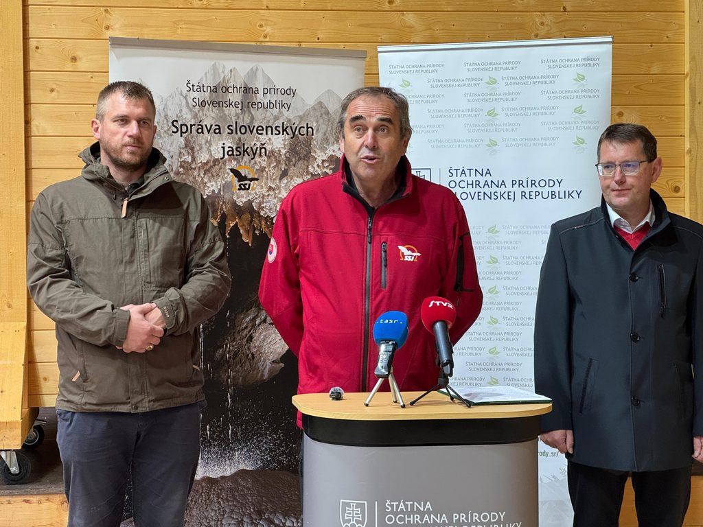 Tlačový brífing pri príležitosti 10. výročia sprístupnenia Brestovskej jaskyne. Traja zástupcovia organizátorov stoja pred bannermi Správy slovenských jaskýň a Štátnej ochrany prírody SR, pred nimi sú mikrofóny médií.