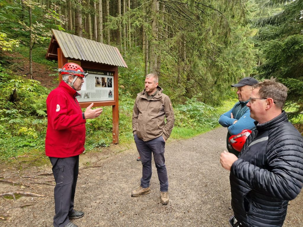 Pracovník Správy slovenských jaskýň podáva výklad účastníkom podujatia pri informačnom paneli Brestovskej jaskyne v lesnom prostredí.