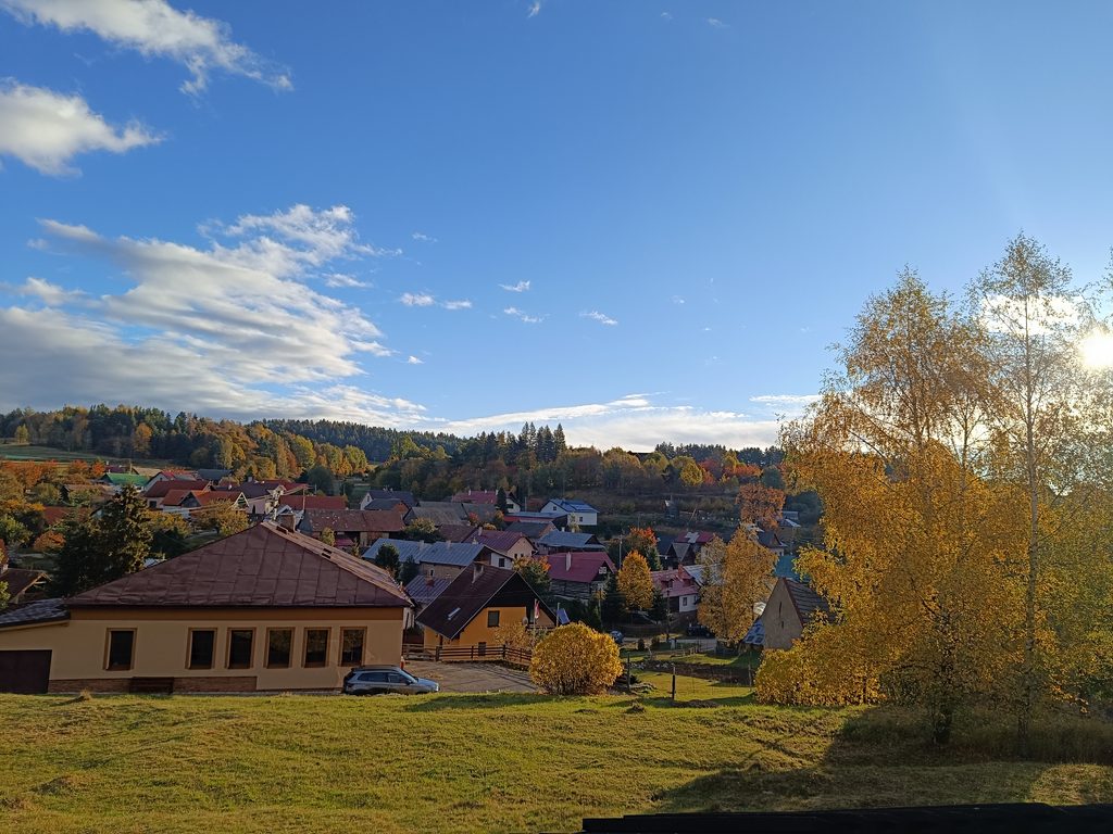 Jesenný pohľad na obec obklopenú farebnými stromami pod modrou oblohou.